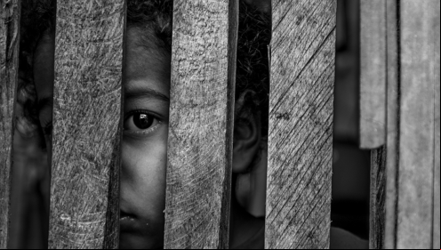 Foto em preto e branco de uma criança atrás de grades de madeira, para representar vítimas de violência sexual