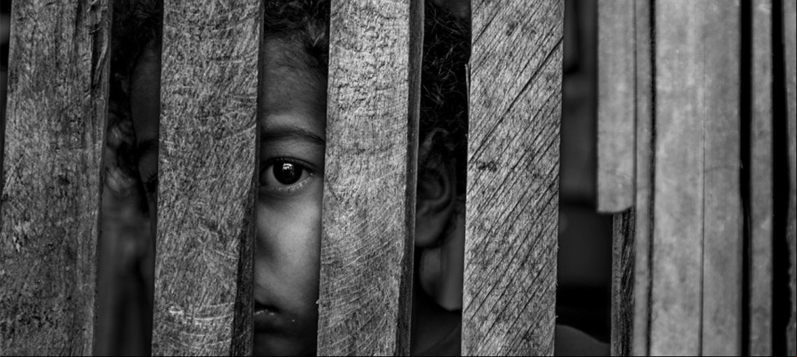 Foto em preto e branco de uma criança atrás de grades de madeira, para representar vítimas de violência sexual